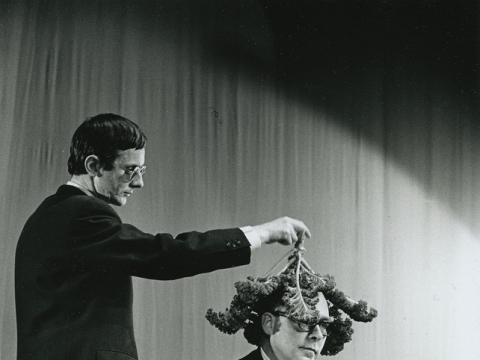 Willem de Ridder dengia Emmetto Williamso galvą kopūsto lapais Robert‘o Filliou performanse „13 Façons d’employer le crâne d’Emmett Williams", Kleine Komedie teatras, Amsterdamas, 1963 m. gruodžio 18 d., fotografija: Dorine van der Klei